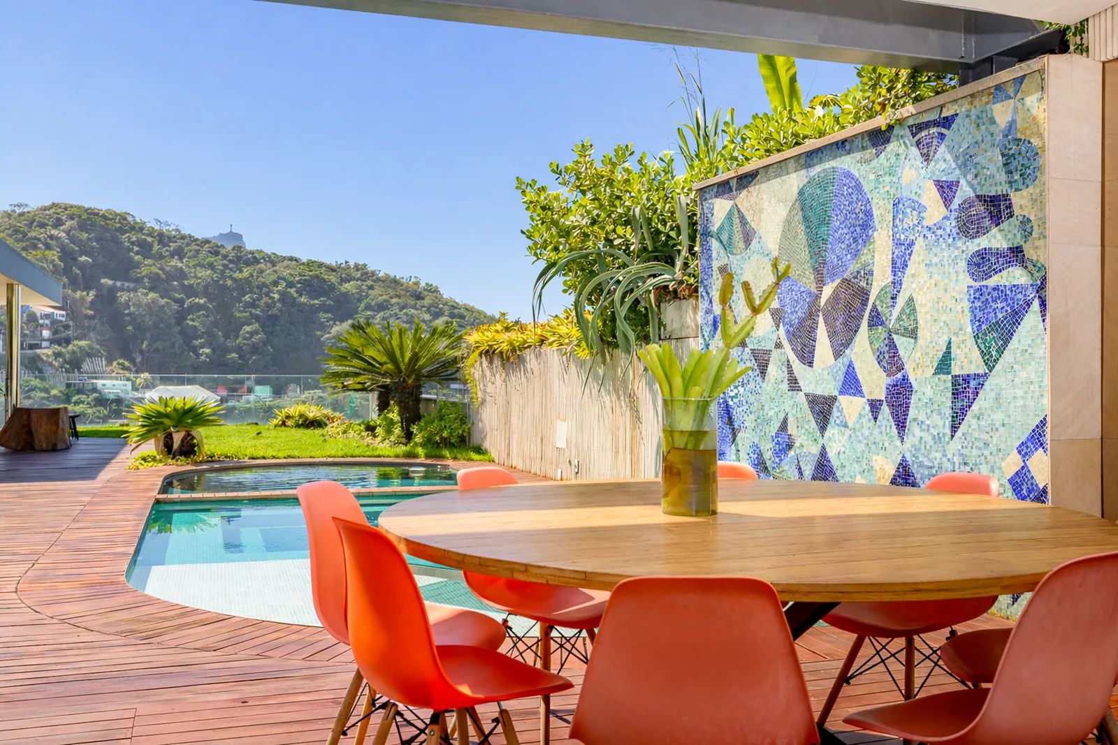 Mesa de comedor al aire libre frente a la piscina, mural de mosaico detrás